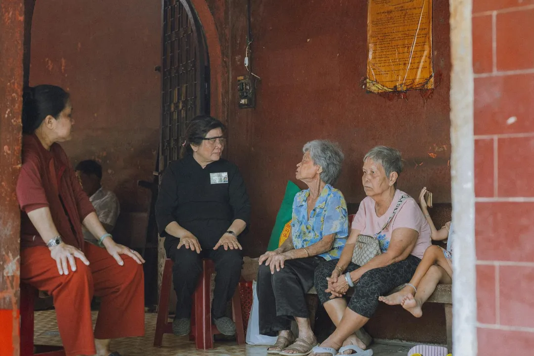 A diverse group of adults seated and conversing with a facilitator in a shaded outdoor courtyard.