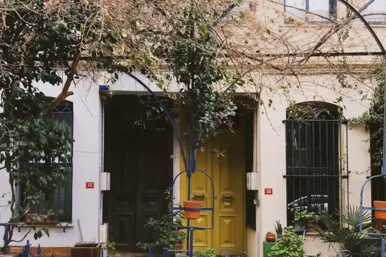 Front view of a small townhouse entry with two doors, decorative plants, and climbing vines over a tree, representing HOA-managed residential housing.