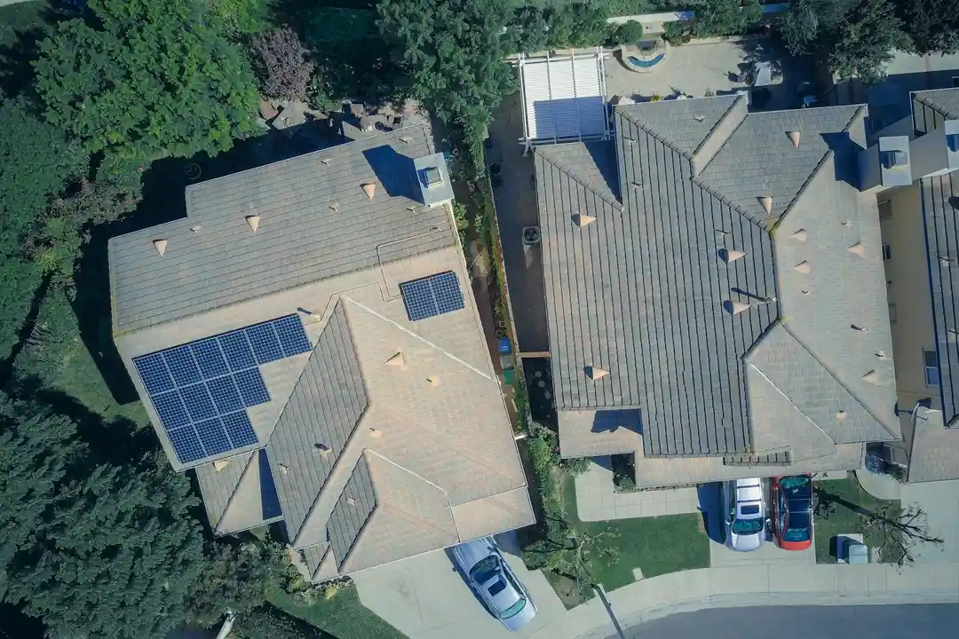 Aerial view of two suburban houses with solar panels on their roofs along a curved street.