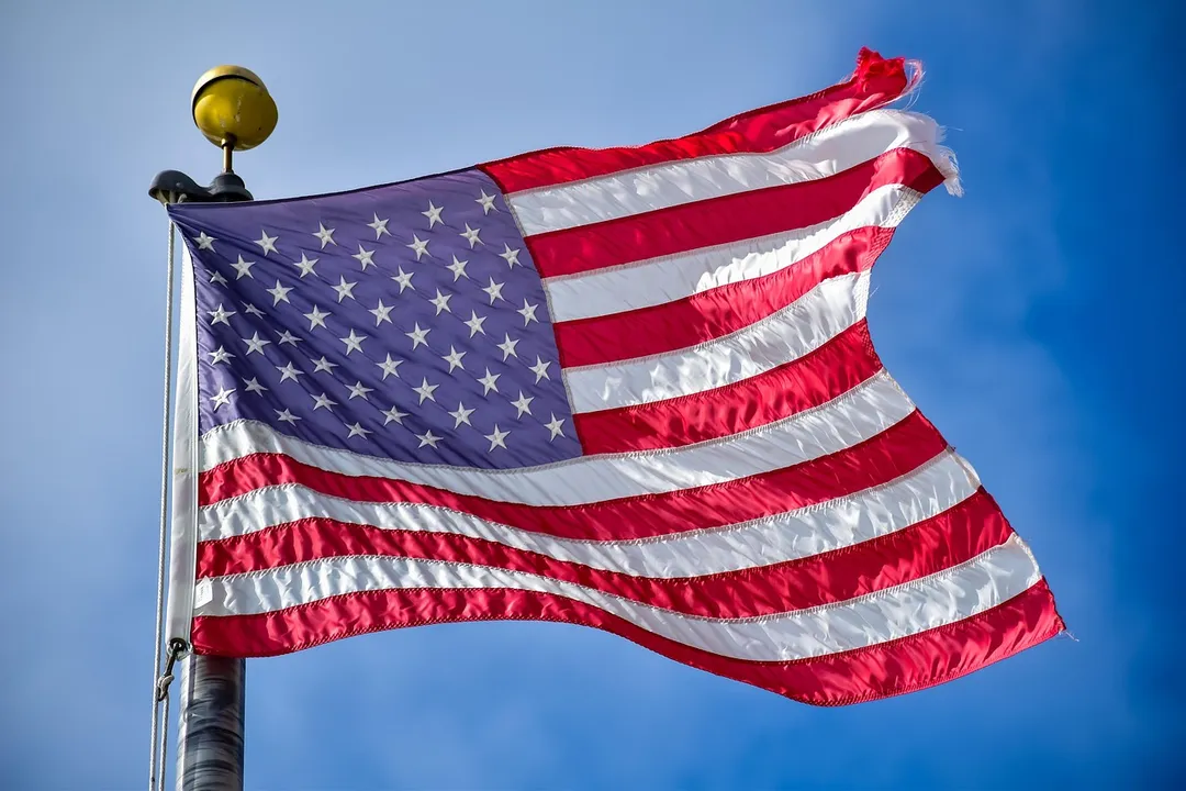 American flag waving on a flagpole with a gold-colored finial against a clear blue sky.