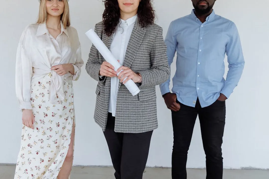 Three professionals standing against a neutral background, one holding rolled blueprints, ready to discuss an architectural project timeline.