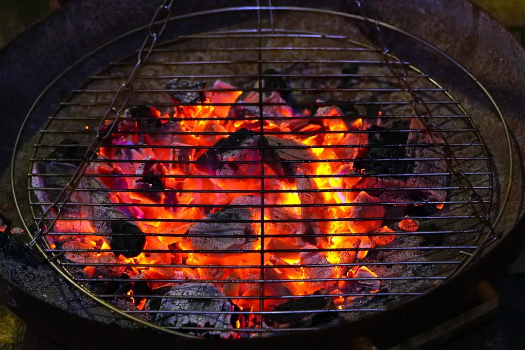 Circular outdoor barbecue grill with a metal grate and bright orange embers.
