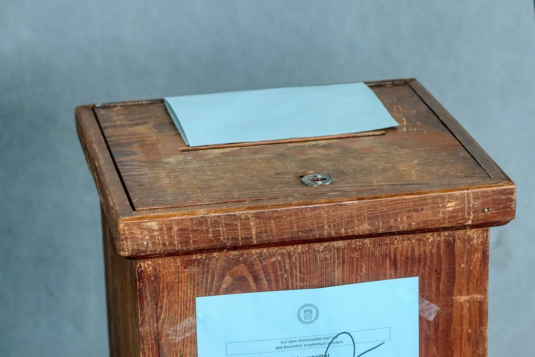A wooden ballot box with a blue slip of paper resting on top, symbolizing voting and formal recall procedures for HOA boards.
