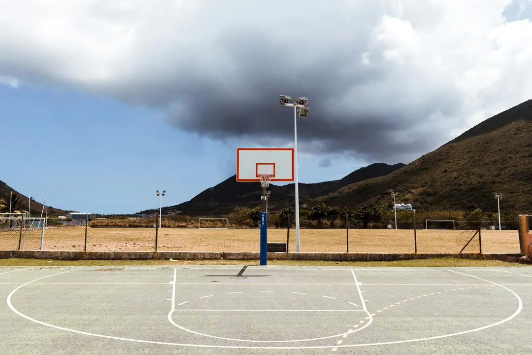 Outdoor basketball court in a desert landscape with a single hoop and a dark, stormy sky.