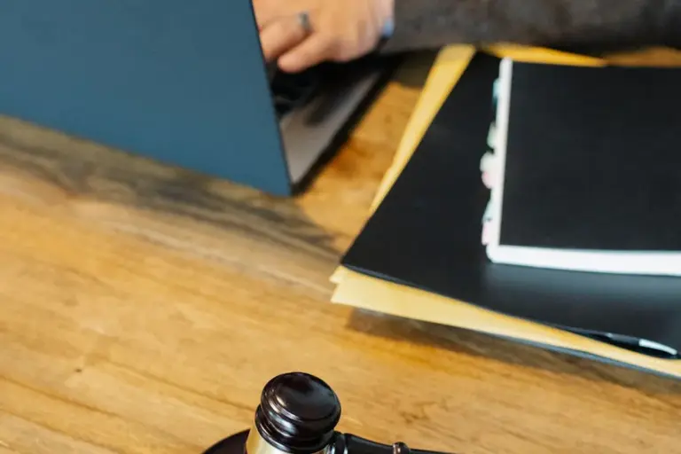 Close-up of a gavel on a wooden desk with folders and a laptop in the background.