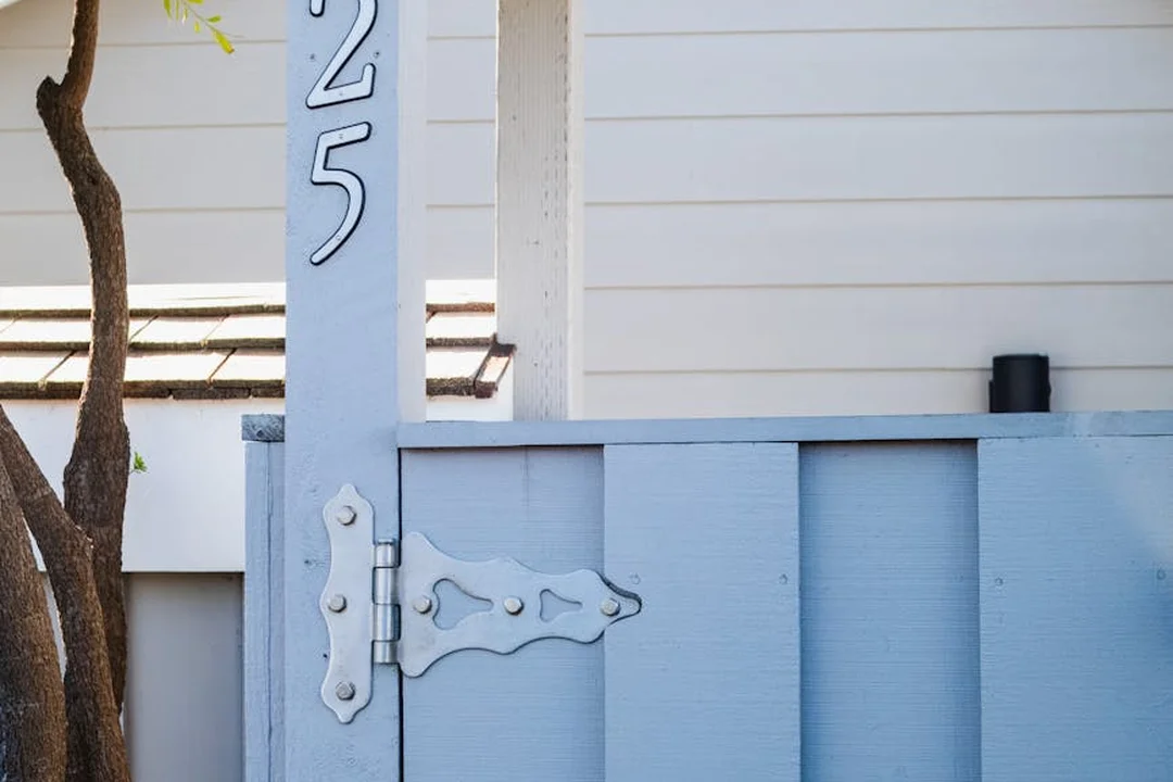 Light blue wooden gate with a metal latch in front of a white house siding