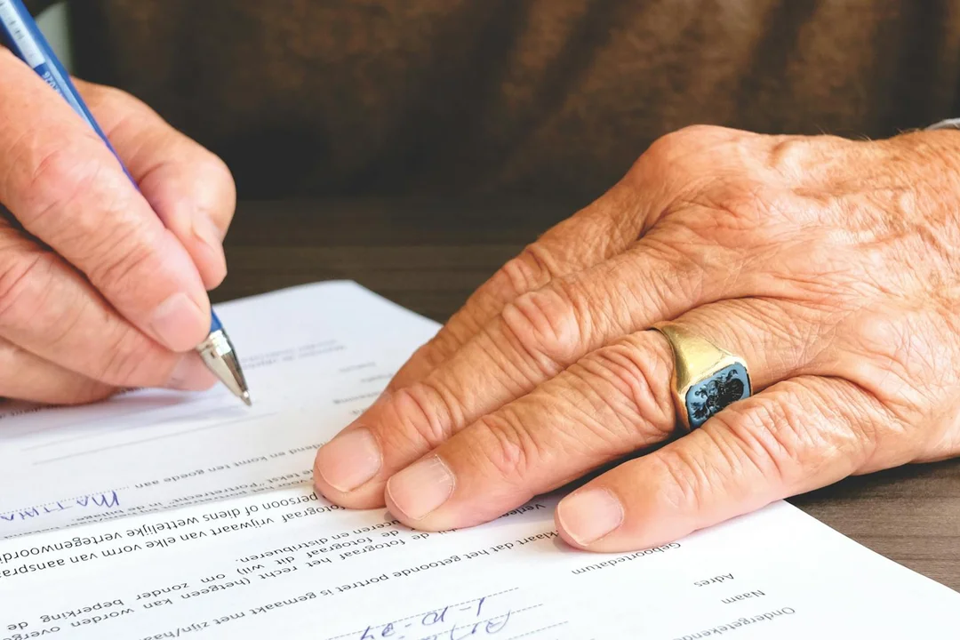 Close-up of a hand signing a document with a pen, wearing a ring, symbolizing legal protections for HOA board members.