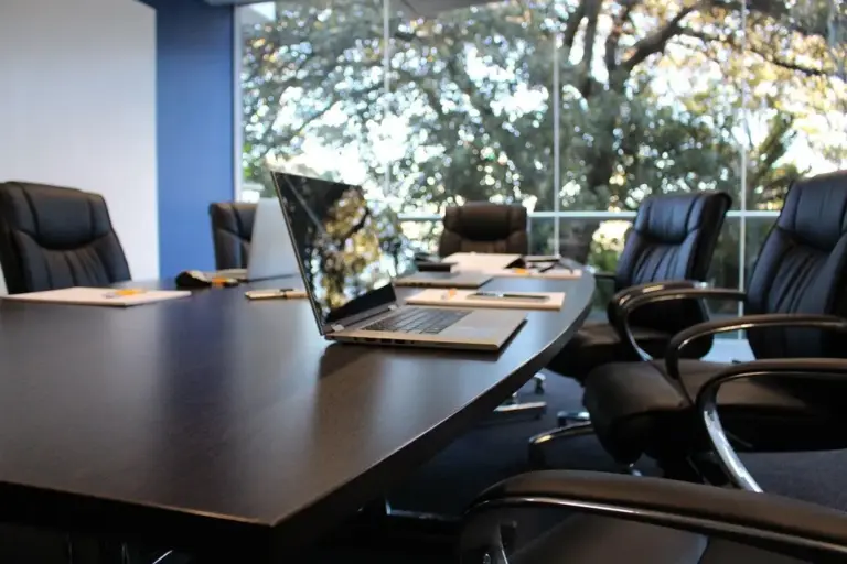 Empty boardroom with a long conference table, laptops, and high-backed chairs set up for an HOA meeting.