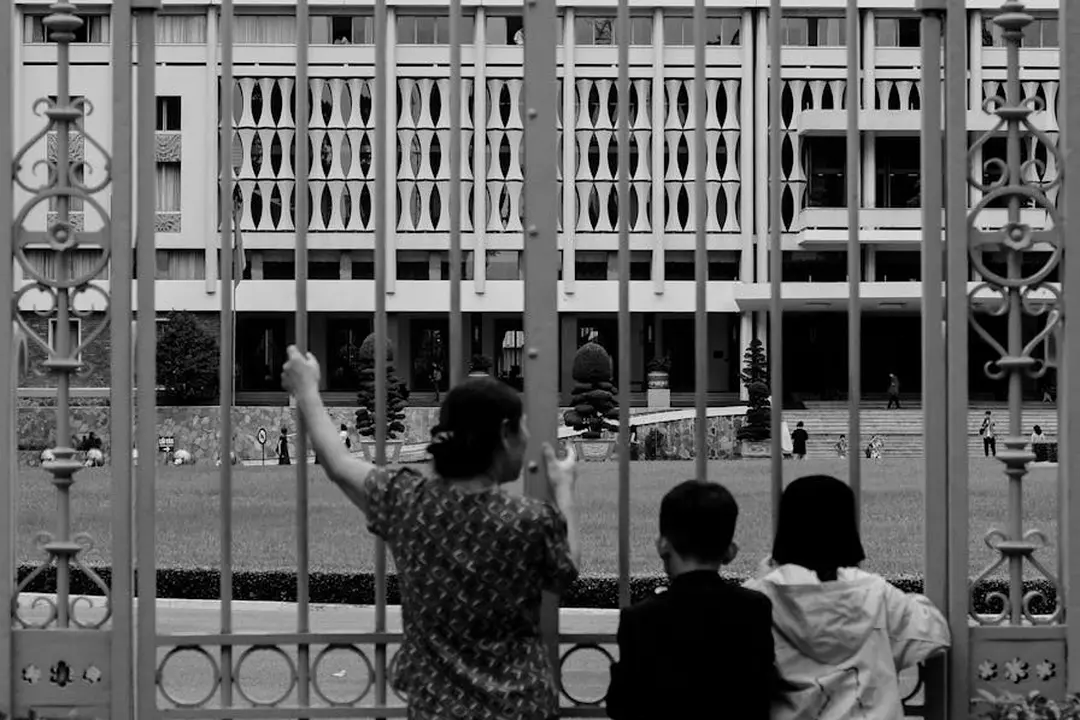 Three people standing by a decorative metal fence and looking toward a modern building.