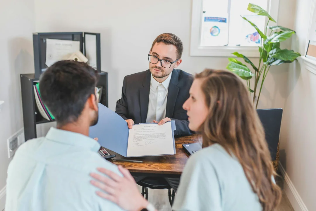 Attorney in a suit explains the differences between bylaws, CC&Rs, and rules and regulations to two clients during a consultation in a small office.