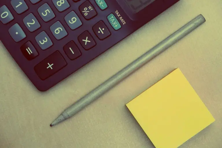 Close-up of a calculator, a pencil, and a yellow sticky note on a desk, representing financial planning for HOA fees.