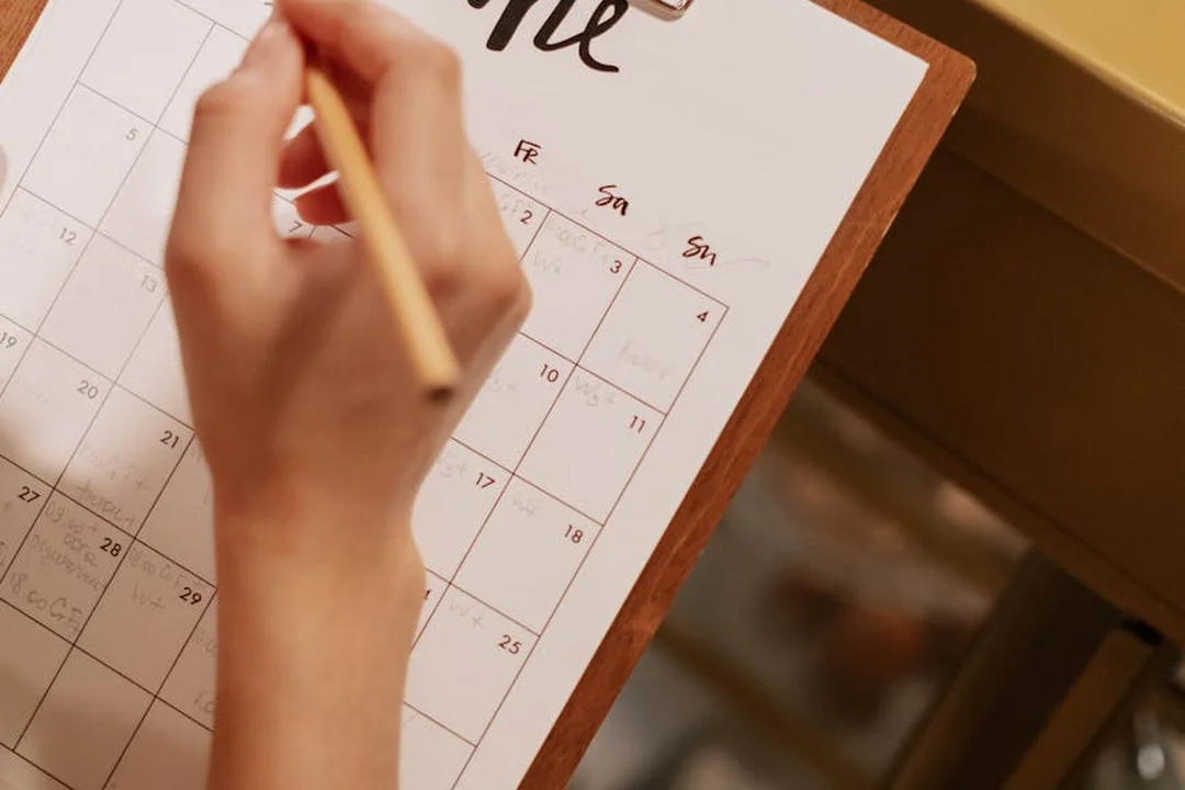 Close-up of a hand writing on a calendar on a clipboard, planning HOA payment due dates.