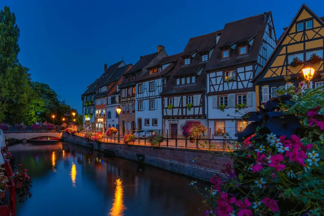 Twilight canal-side street with timber-framed houses and flowering plants along a calm waterway.