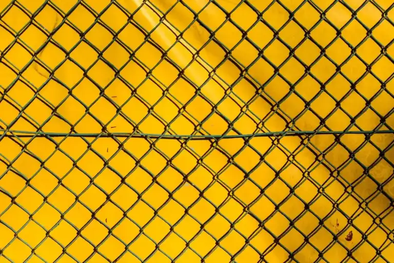 Close-up of a diamond-pattern chain-link fence with a bright yellow background.