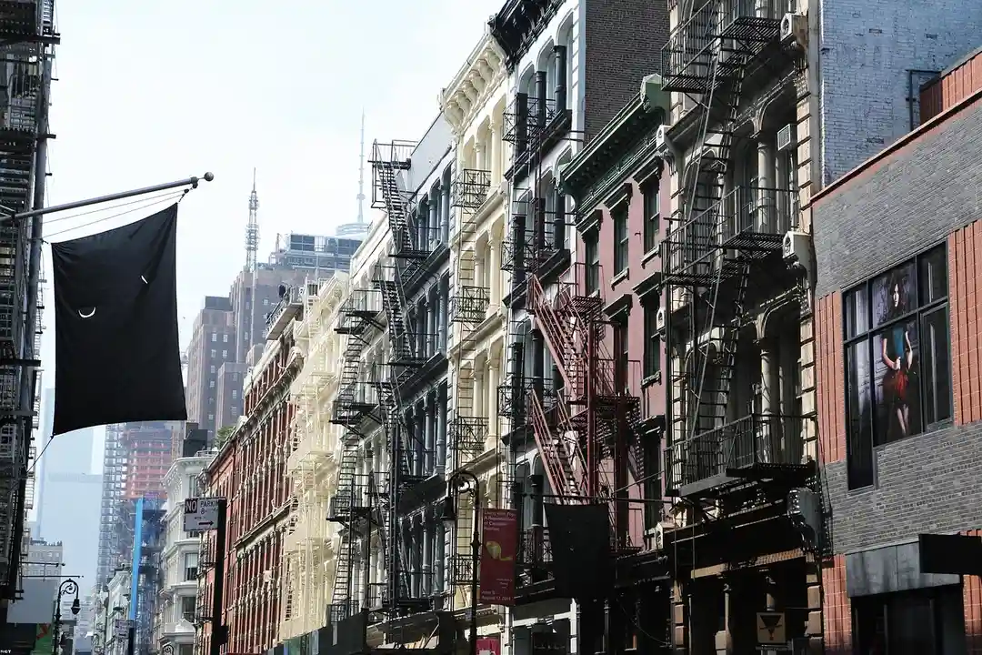 A narrow city street lined with colorful brick row houses and fire escapes on a sunny day.