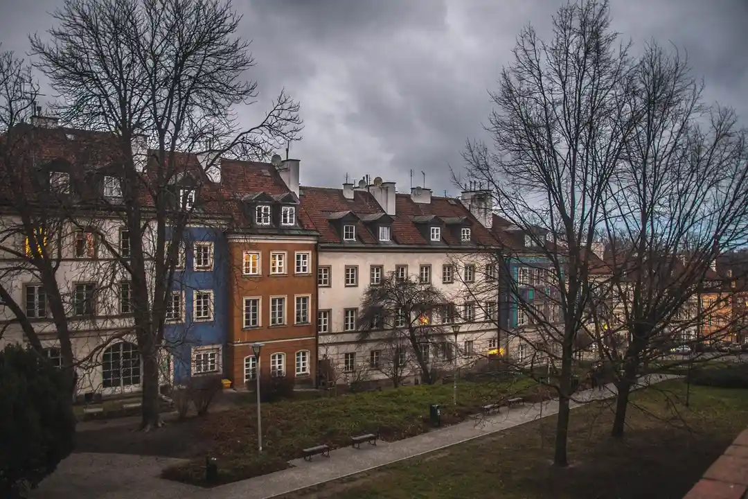 Row of colorful townhouses on a tree-lined street with bare trees and a cloudy sky