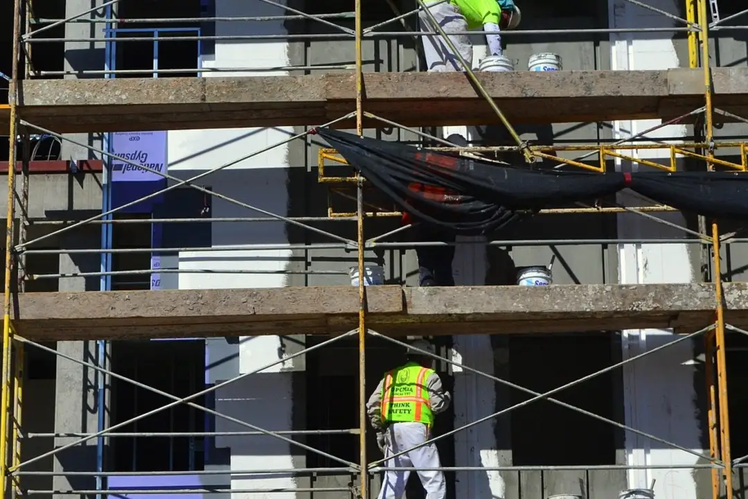 Workers in safety vests standing on scaffolding around a multi-story building under construction.