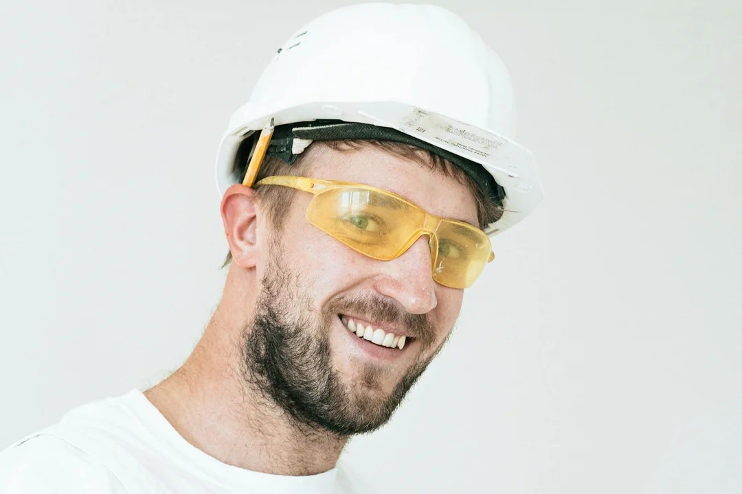 Smiling construction worker wearing a white hard hat and yellow safety glasses