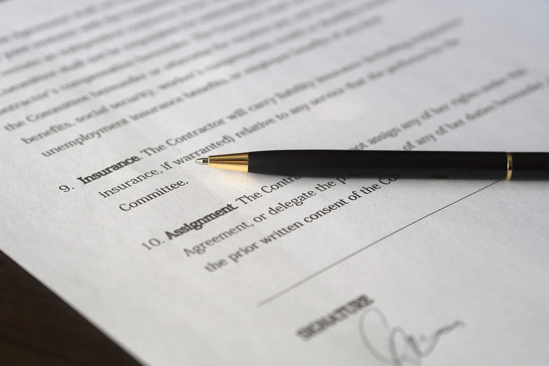Close-up of a legal document with a black fountain pen resting on it, showing headings such as Insurance and Assignment.