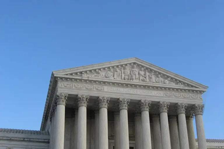 Front view of a grand courthouse with tall stone columns and a triangular pediment against a clear blue sky.