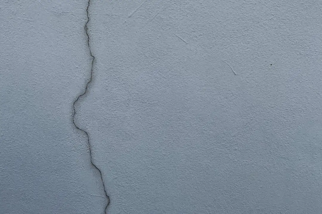 Close-up of a crack in a blue-gray exterior wall, symbolizing maintenance neglect.