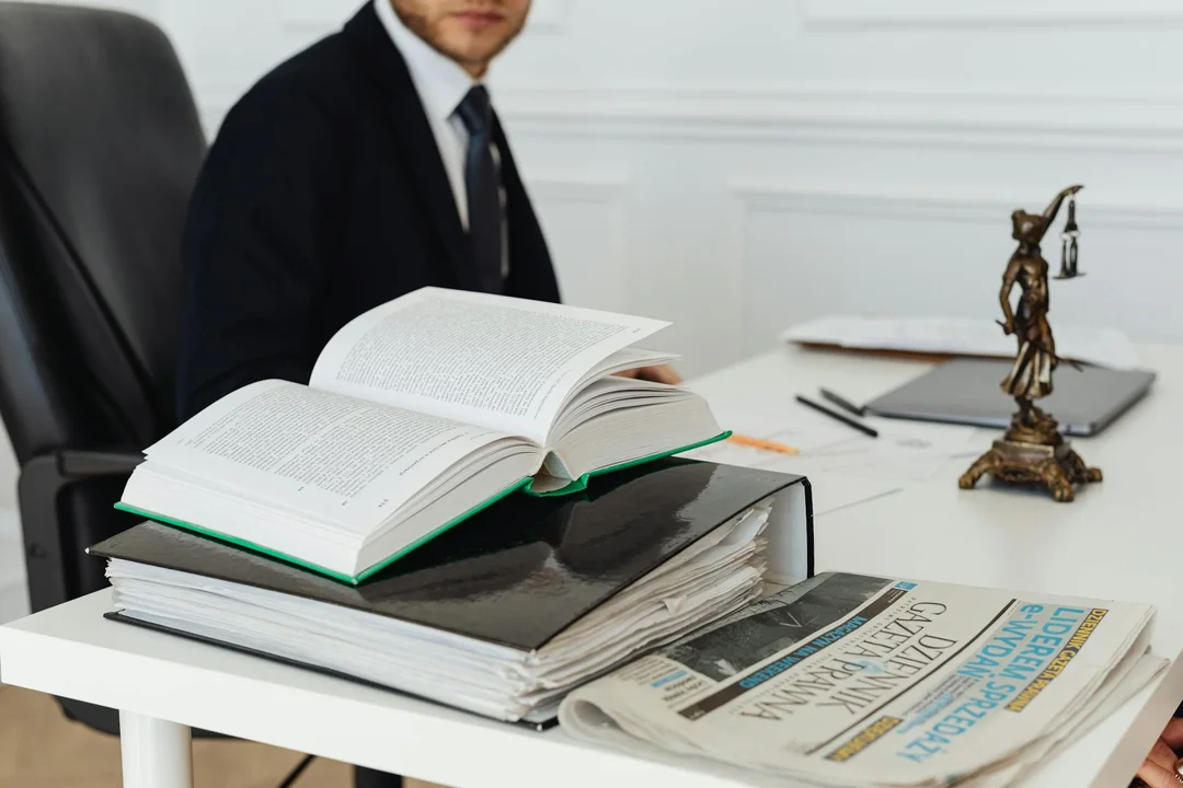 A person in a suit sits at a desk with open law books, a gavel statue, and a newspaper, illustrating the enforcement process for HOA covenants, conditions, and restrictions.