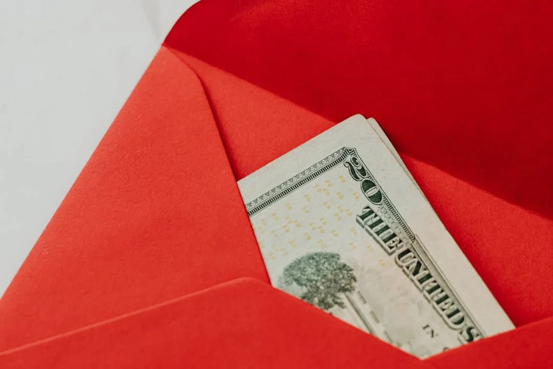 Red envelope with a partial view of a $100 bill peeking out, symbolizing HOA fee costs and financial planning.