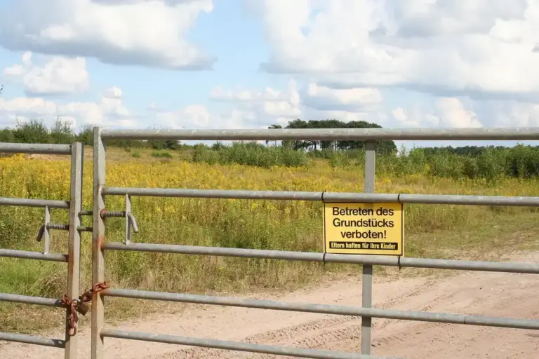 Metal gate with a 'Betreten des Grundstücks verboten' sign in front of an open field.