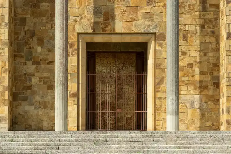 Stone facade with a closed barred metal door at the top of concrete steps