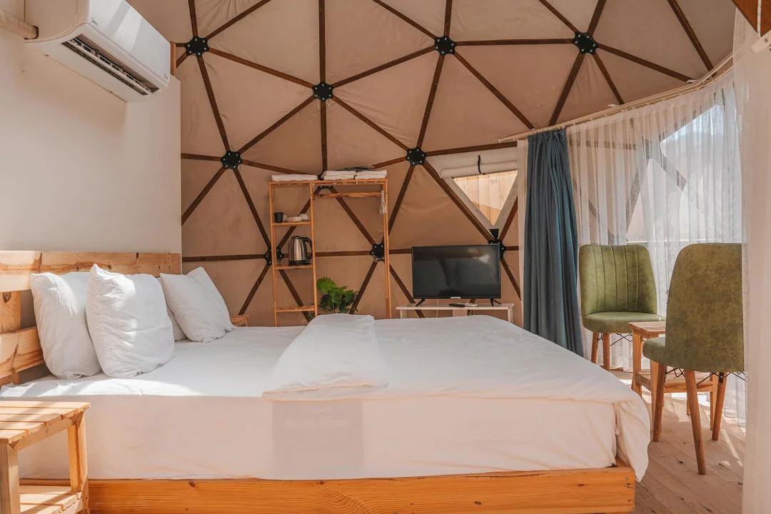 Geodesic-dome bedroom interior with a wall-mounted air conditioner, a bed, desk, and seating area, showcasing HVAC placement in a unique home.