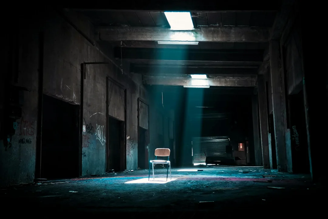 A lone chair sits in a dim, abandoned hallway lit by a narrow beam of light, evoking a ghost town atmosphere.