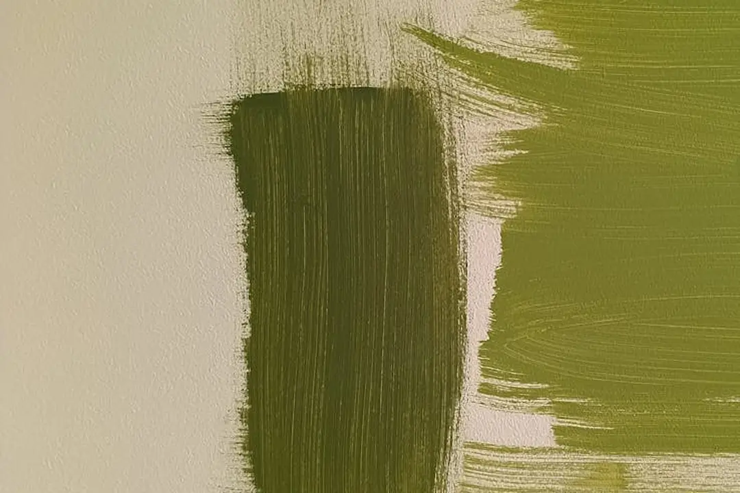 Close-up of olive green paint being brushed onto a light beige wall