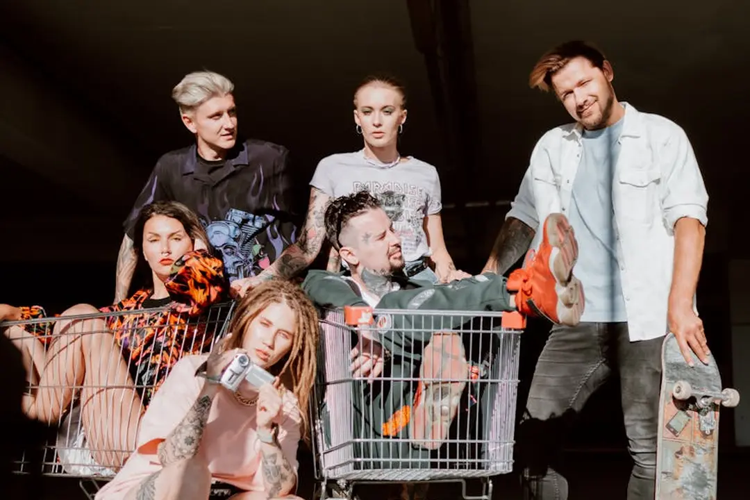 Six young adults posing around and inside a shopping cart in an urban setting, dressed casually, capturing a rebellious, urban vibe.