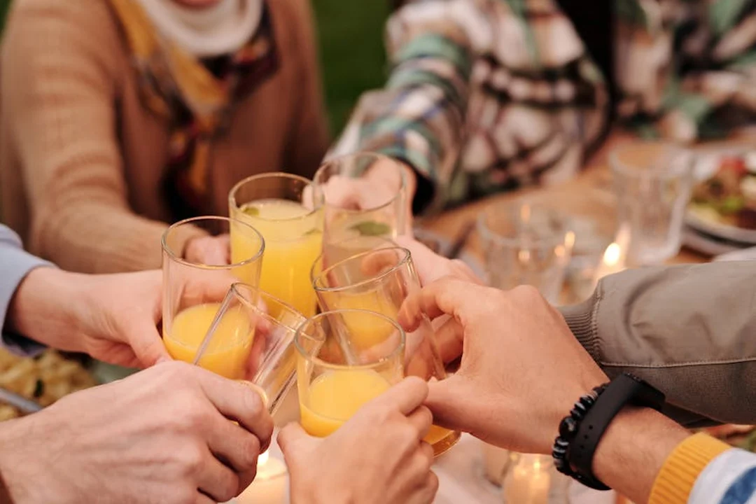 A group of people clinking glasses with orange juice at a table, candles in the background, suggesting a social gathering in a community setting.