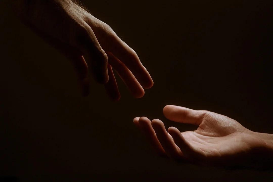 Two hands reaching toward each other in a dark background, symbolizing connection in HOA facilities.