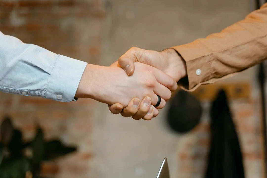 Two people shaking hands over a contract review session with a laptop nearby, symbolizing partnership in selecting an HOA management company.