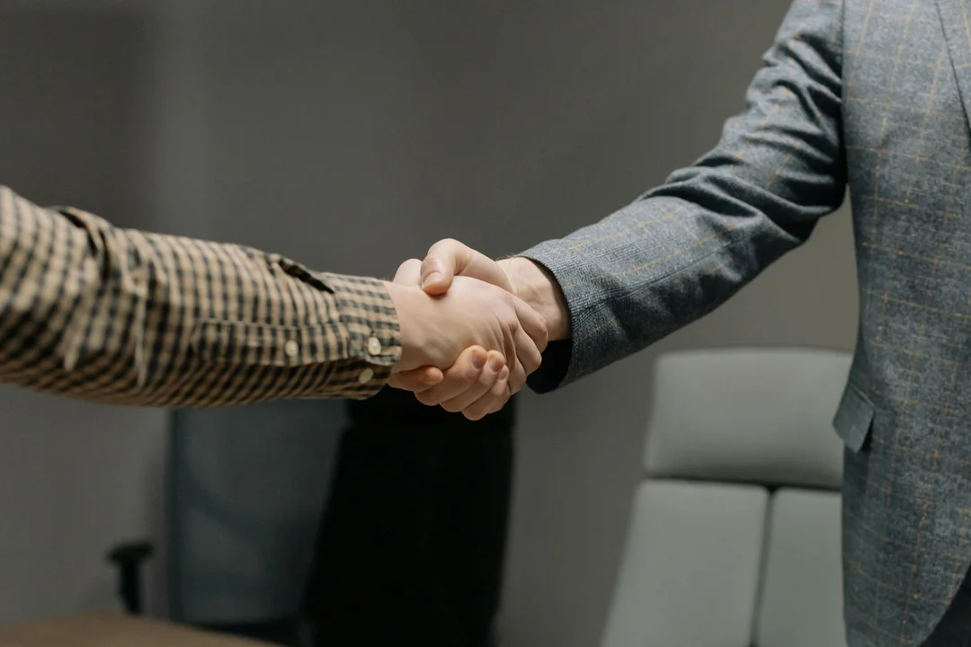 Two professionals in business attire shake hands in a conference room.