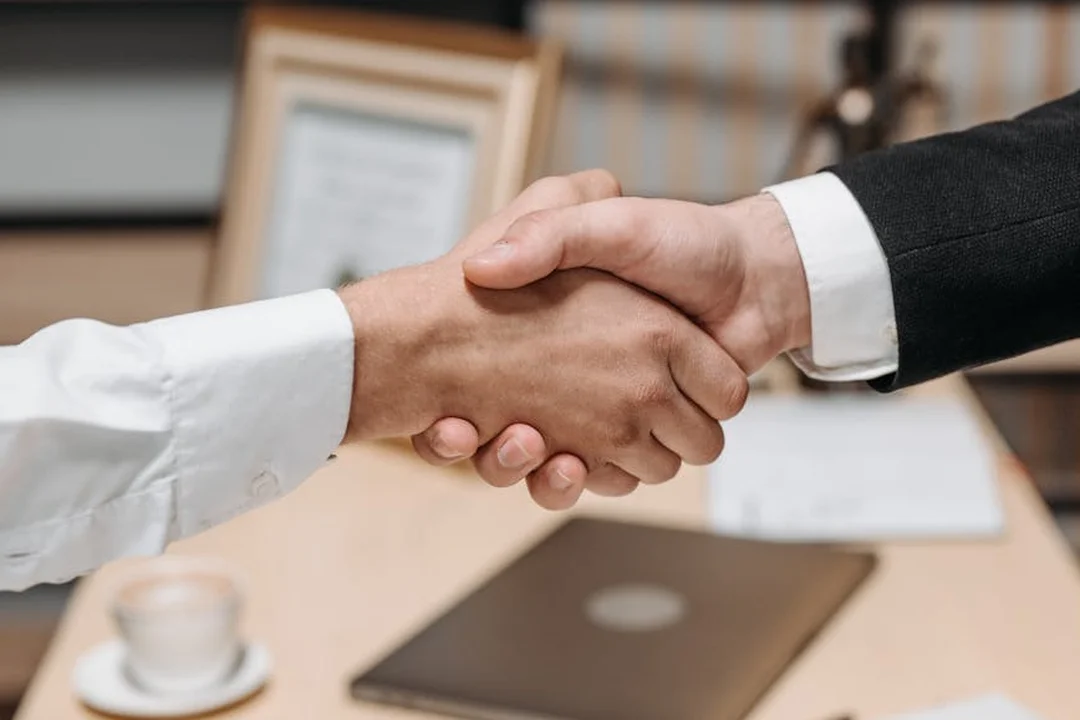 Handshake between two professionals over a desk with documents, symbolizing agreement and indemnification discussions.