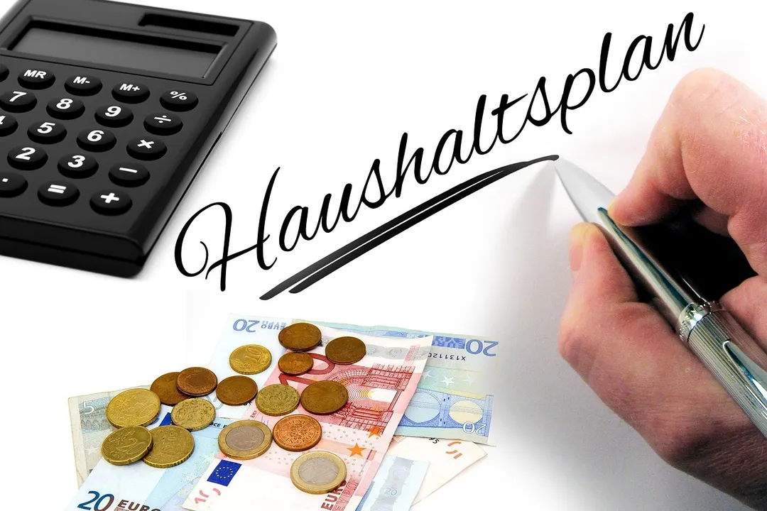 Budget planning with a calculator, coins and banknotes, and a hand writing on a page labeled Haushaltsplan
