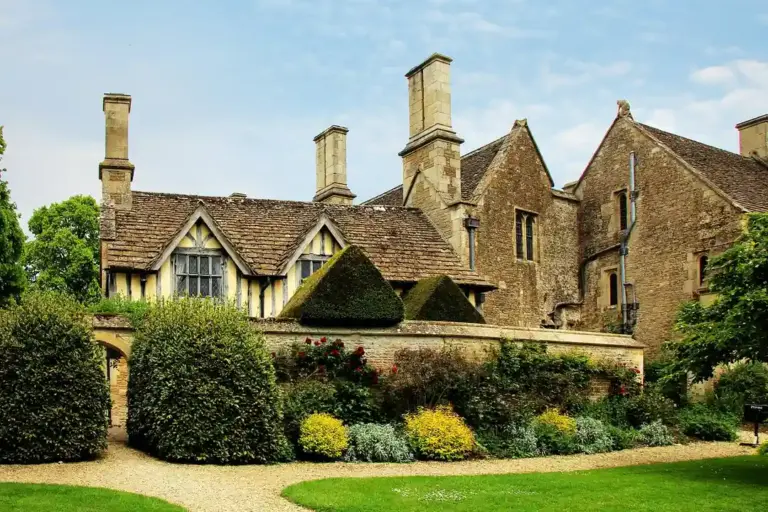 Stone manor with manicured hedges and a gravel driveway under a blue sky
