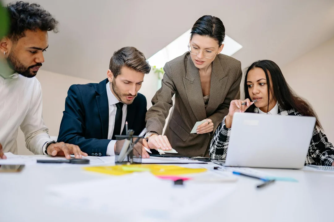 A diverse team of professionals gathered around a table, examining documents and a laptop as they prepare to open an HOA bank account.