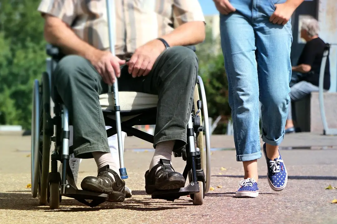A person in a wheelchair and a neighbor walking outdoors, highlighting accessibility and inclusion in housing communities