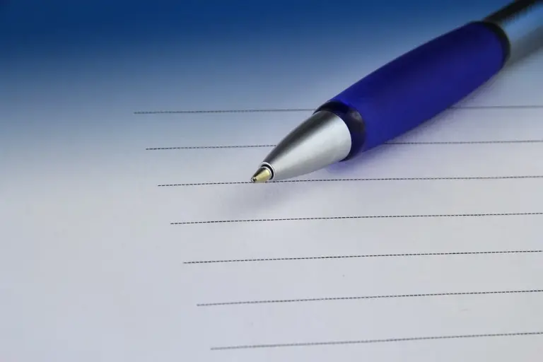 Blue ballpoint pen resting on lined white paper, ready for drafting notes.