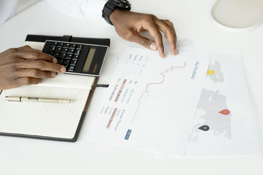 Close-up of hands with a calculator, notebook, and printed documents on a desk while reviewing applicant background data.