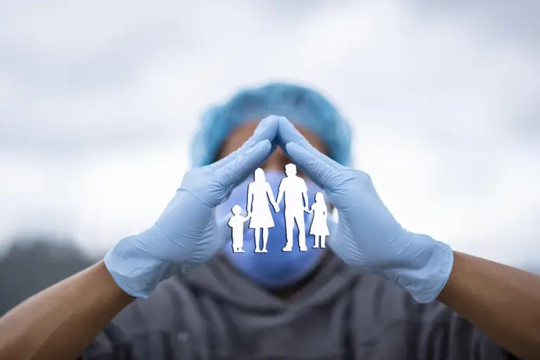 A person wearing blue gloves forms a protective triangle around a paper cut-out of a family, symbolizing protection and risk management for HOA boards.