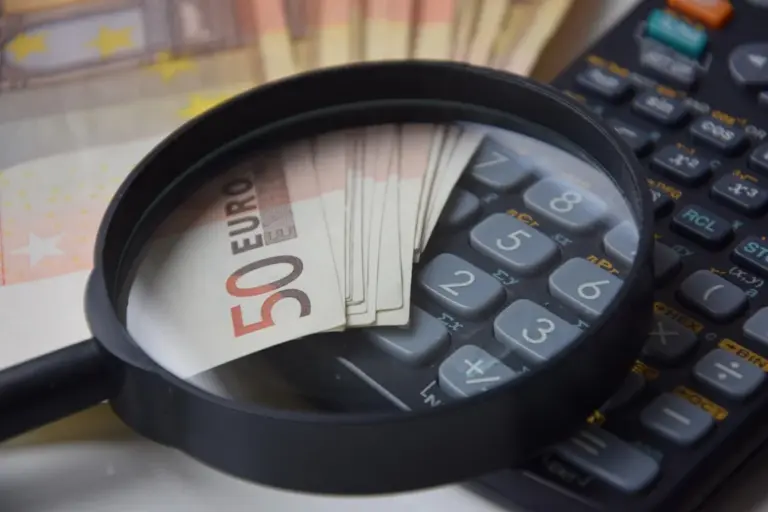Close-up of a magnifying glass over euro banknotes and a calculator, illustrating careful budgeting for an HOA