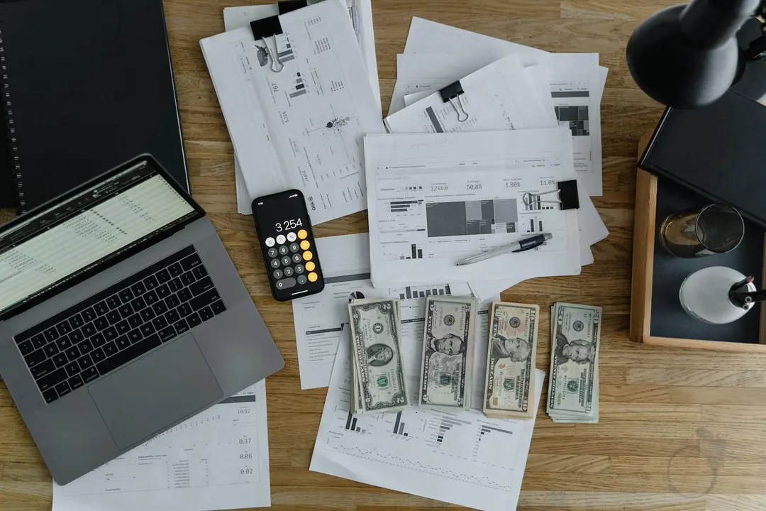 Desk with a laptop, calculator, scattered receipts and documents, and stacks of currency illustrating budgeting for an HOA.