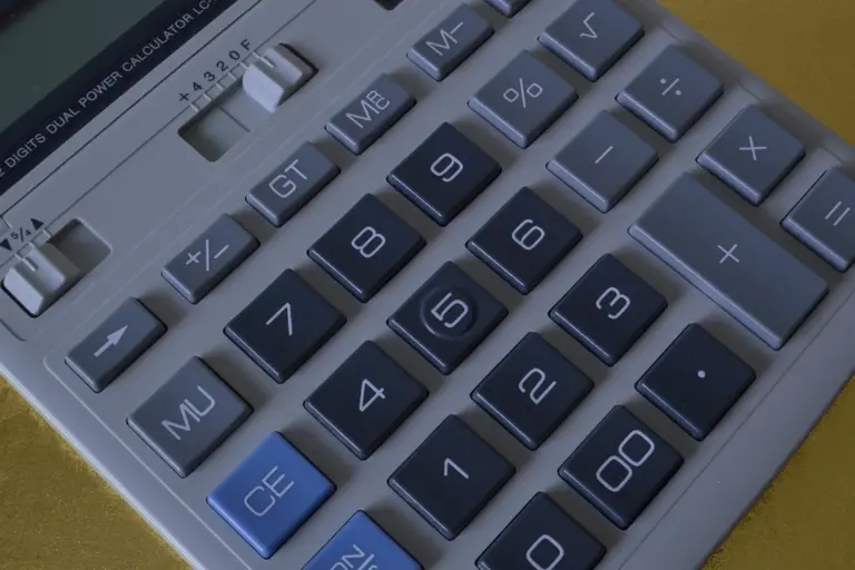 Close-up of a gray calculator with blue and gray buttons on a yellow surface.