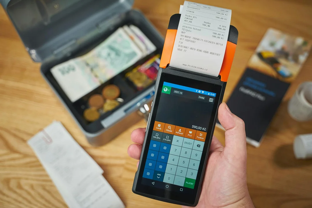 Handheld card reader with a receipt printer, a cash box with bills, and payment-related materials on a wooden surface, illustrating financial transactions for HOA fees.