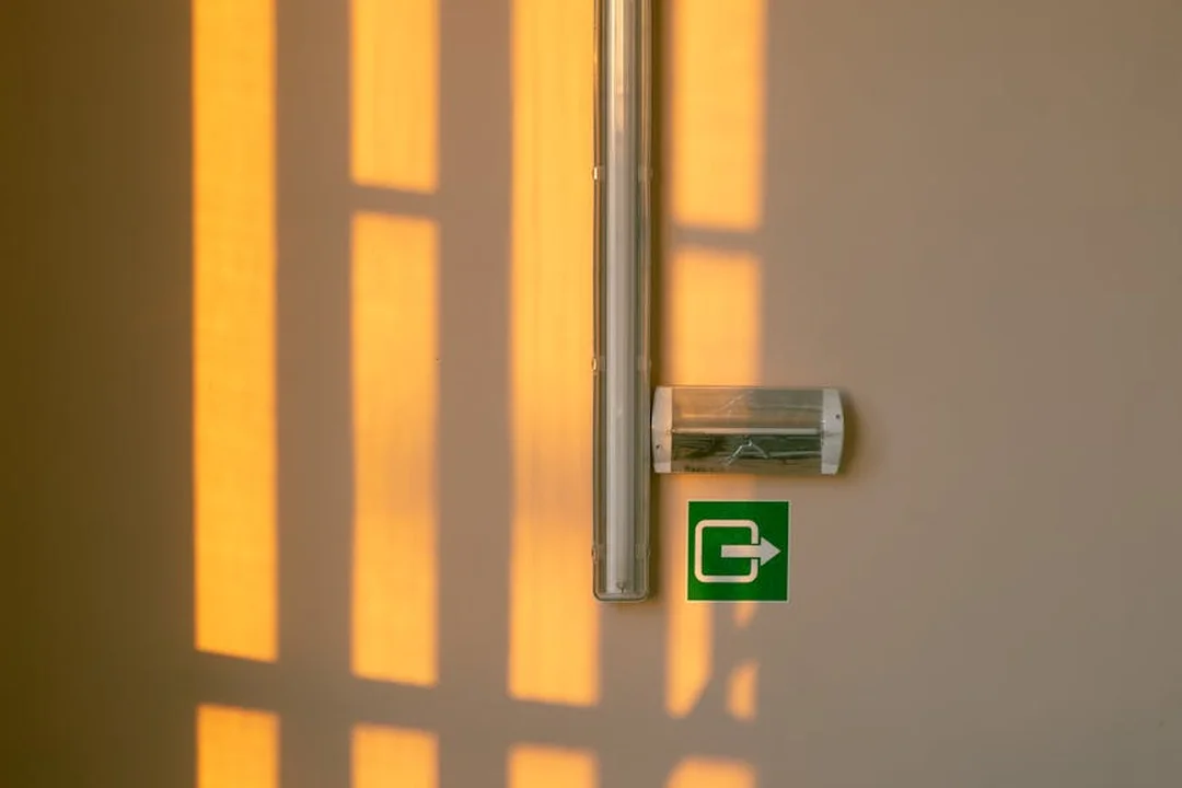 Exit door with lever handle and a green emergency exit sign on a wall, with warm vertical light patterns cast across the surface